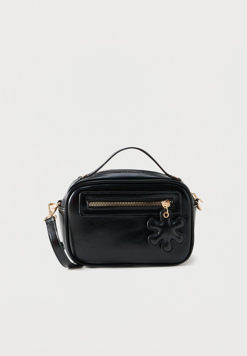 Sac bandoulière compact en cuir noir avec fermeture éclair dorée, petite poignée supérieure, sangle amovible et breloque noire en forme de fleur sur la poche avant.