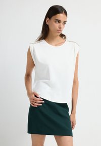 Witte mouwloze top met juweelversieringen op de schouders, gecombineerd met een donkergroen minirok. Soepele textuur, ontspannen pasvorm.