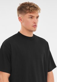 Czarna bawełniana koszulka z okrągłym dekoltem, krótkimi rękawami i luźnym krojem. Gładka tekstura bez widocznych wzorów czy akcentów.