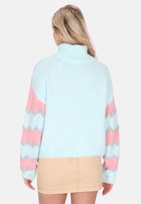 Lichtblauwe trui met hoge kraag; heeft roze en grijze chevronstrepen op de mouwen; zacht, gestructureerd materiaal; cropped ontwerp.
