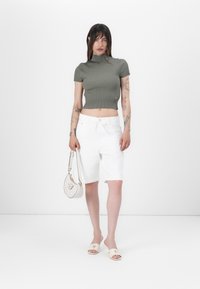 Grünes geripptes Top mit kurzen Ärmeln, weiße knielange Shorts, weiße Tasche mit Riemen, cremefarbene Slippers. Minimalistisches Design, glatte Texturen.