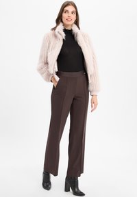 Veste en fausse fourrure rose clair, col roulé noir, pantalon marron taille haute et bottines à talons noires. Textures lisses et coupe ajustée.