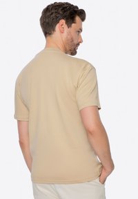 Beige tričko s krátkým rukávem vyrobené z hladkého materiálu, s jednoduchým designem, kulatým výstřihem a rovný střih. Žádné viditelné vzory ani loga.