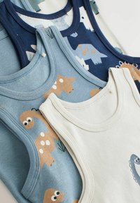 Pile de quatre débardeurs pour tout-petits en bleu, marine et crème avec des dinosaures dessinés en différentes couleurs et motifs.