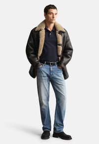 Czarna skórzana kurtka z beżowym kołnierzem z baranka, granatowa koszulka polo, jasnoniebieskie dżinsy i czarne botki. Codzienny strój o dopasowanym kroju.