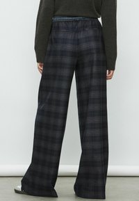 Brede, marineblauwe geruite broek met een elastische tailleband. Bevat een gemêleerd ruitpatroon met subtiele blauwe en grijze accenten.