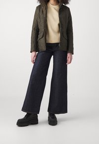 Olive quilted jacket with a hood, beige sweater, and wide-leg dark denim jeans. Black platform shoes with textured soles.