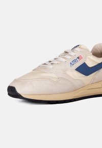 Sneaker in suede beige con accenti blu, dettagli in rete e suola in gomma nera. I lacci sono bianchi, con branding sul lato e sulla linguetta.