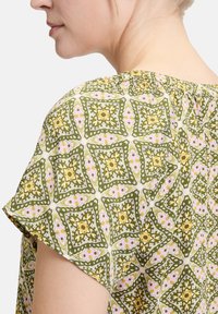 Bluzka w zielono-różowy wzór z geometrycznym florystycznym designem, z krótkimi rękawami, wykonaną z miękkiego, lekkiego materiału o delikatnej teksturze.