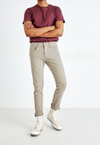 Camiseta granate con un pequeño logo, combinada con unos vaqueros beige claro y zapatillas altas color crema. Los vaqueros son ajustados y con puños remangados.