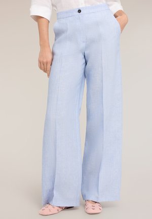 Lichtblauwe wijde broek met plooien aan de voorkant, gecombineerd met lichtroze geborduurde ballerina's, zichtbare witte overhemdsmouwen.