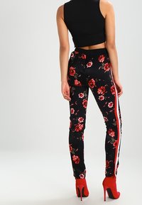 Květinové černé kalhoty s červenými akcenty, elastický pas, tapered fit, s výrazným vzorem růží a kontrastními postranními pruhy.
