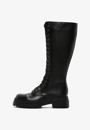 Alti stivali neri in pelle con lacci e suola spessa, texture liscia e dettagli con occhielli lungo il lato per una chiusura sicura.