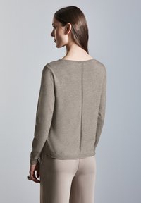 Beige lange mouwtrui met een ronde halslijn, achternaaddetail en geribde manchetten. De stof lijkt zacht met een gladde textuur.