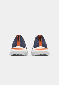 Navy athletic shoes with an orange accent, featuring a textured upper, padded collar, and grey outsole. Rear view highlights streamlined design.