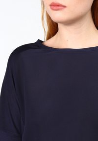 Haut bleu marine à encolure large, tissu doux et manches courtes. Design minimaliste avec une texture lisse, sans motifs ni éléments décoratifs visibles.