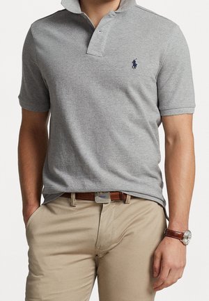 Graues Poloshirt mit Kragen, kurzen Ärmeln und einem navyblauen Logo auf der Brust. Tragen mit beigen Chinos und einem braunen Ledergürtel.