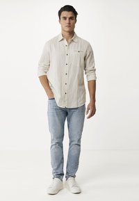 Lichtgestreepte overhemdbloes met een borstzak, gecombineerd met lichtblauwe jeans en witte sneakers. Eenvoudig ontwerp en casual stof.