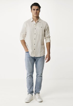 Camisa de botón a rayas claras con un bolsillo en el pecho, combinada con jeans claros y zapatillas blancas. Diseño simple y tejido casual.