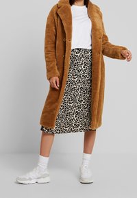 Brun faux fur frakke med reverskrave, knaplukning, parret med en leopardprint midi skirt og hvide sneakers med grå detaljer.