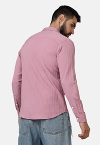 Maglietta lunga a maniche con coste rosa, caratterizzata da un colletto classico e polsini con bottoni, abbinata a pantaloni in denim blu chiaro.
