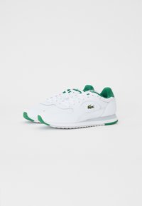 Sneaker atletici bianchi con accenti verdi, realizzati in pelle e rete, con design a lacci, suola testurizzata e logo del marchio.