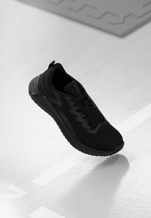 Chaussure de sport noire avec un dessus en mesh texturé, dotée d'un système de laçage, d'une semelle rembourrée et d'une languette à l'arrière pour un enfilage facile.
