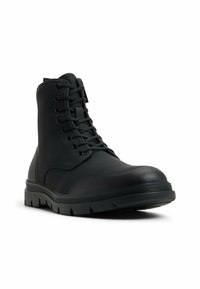 Botín negro impermeable hasta el tobillo con un acabado liso y mate. Presenta puntera redonda, cordones redondos y una suela de goma resistente con un dibujo pronunciado.