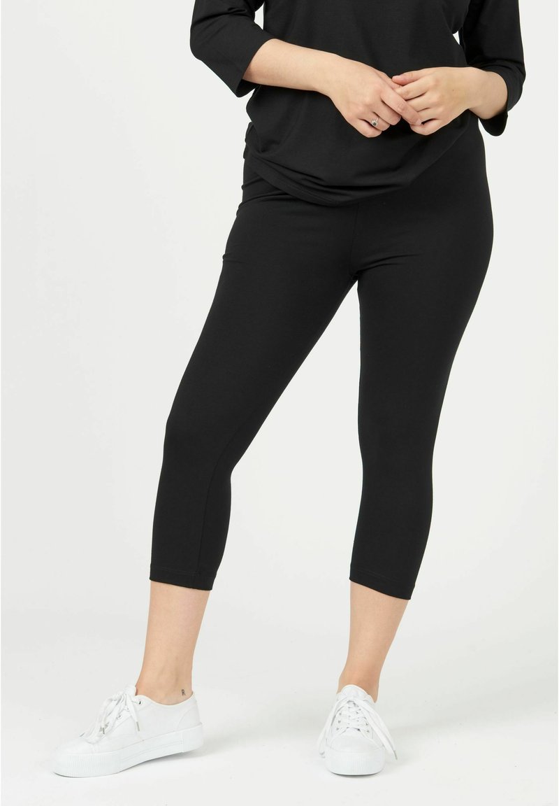 Black capri leggings made from stretchy fabric, featuring a smooth texture and a fitted design. Worn with white sneakers.