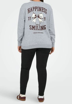 Personne portant un sweat-shirt gris avec un nœud blanc et le texte « Bonheur 1991 Continuez à sourire Une bonne journée pour gagner » au dos, pantalon noir.