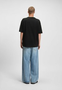 Camiseta negra de tamaño grande con mangas cortas, combinada con jeans de pierna ancha en azul claro. Textura suave, diseño minimalista y sin logotipos visibles.