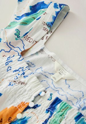 Valge linase kleidi rihm, millel on värvikas trükitud kaardimuster, väikesed valged nööbid ja nähtav kangasilt kaeluse sees.