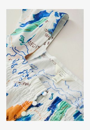 Valge linase kleidi rihm, millel on värvikas trükitud kaardimuster, väikesed valged nööbid ja nähtav kangasilt kaeluse sees.