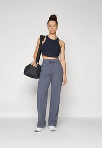 Tumši zils īss topiņš un pelēkas brīva piegriezuma bikses ar auklu, kombinēts ar melnu plecu somu un baltām sporta kurpēm.