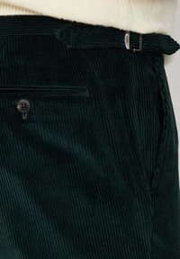 Tmavozelené kordové nohavice so štruktúrovaným povrchom, pútkami na opasok a uzatváraním na gombík s malým logom.
