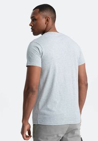Grå kortærmet T-shirt i et blødt, let materiale med en rund hals og en afslappet pasform, set fra ryggen, der fremhæver sømdetaljer.