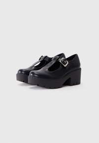 Black leather Mary Jane shoes with a rounded toe, cutout detail, and a chunky platform heel, featuring a silver buckle accent.