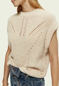 Pull beige clair en maille avec un col côtelé, des manches courtes et des motifs ajourés. Texture douce, doté d'une coupe décontractée avec de subtiles mouchetures.