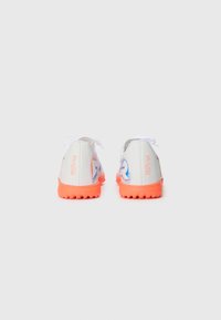 Une paire de chaussures de sport blanches avec des semelles orange vif, arborant le texte "FUTURE" en bleu et orange, vue de l'arrière sur un fond clair.