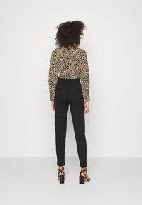 Pantalon noir taille haute avec une silhouette ajustée, associé à un blouse beige imprimé léopard. Stylisé avec des talons strappés noirs.