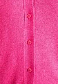 Fucsia kofta med ribbat mönster, som har en rad på fem matchande runda knappar framtill. Mjuk stickad tyg, avslappnad design.