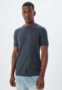 Korte mouw, donkerblauw gebreid sweater met een ronde halslijn en geribbelde manchetten. Gladde textuur met een aansluitend ontwerp. Draag met lichte denim shorts.