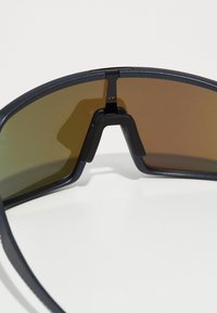 Sonnenbrille mit einem dunklen Rahmen und braun getönten Gläsern. Verfügt über ein einzigartiges, kantiges Design und eine ausgeprägte Nasenbrücke für zusätzlichen Halt.