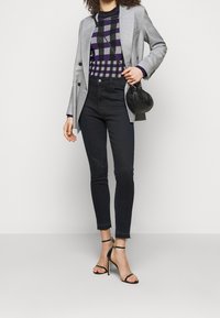 Blazer gris sur mesure porté sur un pull à carreaux violets ; jean skinny noir taille haute avec ourlet effiloché ; talons noirs à brides et petit sac.