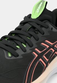 Tênis atlético preto com parte superior texturizada, detalhes verdes e marcação rosa. Apresenta atacadores planos, língua acolchoada e biqueira reforçada.