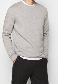 Felpa grigia con logo testurizzato "LES DEUX", collo rotondo e polsini a costine, abbinata a pantaloni neri. Tessuto morbido con una vestibilità casual.
