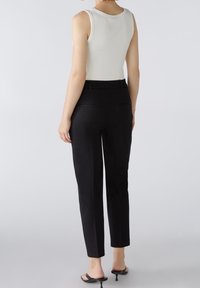 Pantalon noir ajusté avec un design slim-fit, doté de poches arrière et d'une taille élastique, associé à un débardeur blanc à côtes.