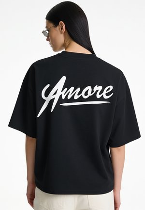Woman with long dark hair wearing sunglasses and a black shirt with white script text "Amore" on the back.