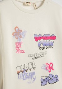 Biały dziecięcy sweatshirt z kolorowym tekstem w stylu graffiti zawierającym napisy "REBEL", "POPROSZĘ, ŻEBYŚ MNIE ZROZUMIAŁ" oraz "TWÓJ WYBÓR", a także rysunki kwiatów.