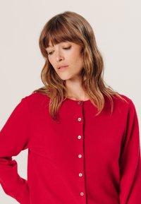 Rote Strickjacke mit Rundhalsausschnitt, langen Ärmeln und sechs vorderen Knöpfen sowie einer glatten Textur. Einfaches Design ohne Muster.